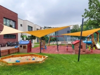 Voiles d'ombrage jaunes sur mesure installées au-dessus d'une aire de jeux moderne avec bac à sable et cabanes pour enfants