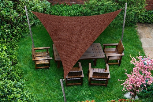 Toldo vela triangular marrón de HDPE sobre muebles de jardín de madera en un césped verde