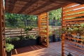 Bruin HDPE vouwgordijn als zonwering gemonteerd op een houten pergola boven een stijlvol terras met planten