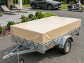 Maßgeschneiderte beige Schutzplane montiert auf einem einachsigen Pkw-Anhänger mit Metallbordwand