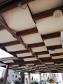 Wasserdichte, beige Premium-Pergolabahn, montiert unter einer Terrassenkonstruktion aus Holz als Sonnenschutz