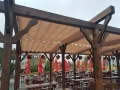 Rulou roman bej impermeabil Premium pe o structură de terasă din lemn cu grădină de vară