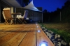 Toldo vela triangular Premium impermeable instalado sobre una terraza de madera con muebles por la noche