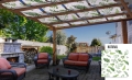 Vattentät paviljongvåd med växttryck monterad på en träpergola över en terrass med utemöbler