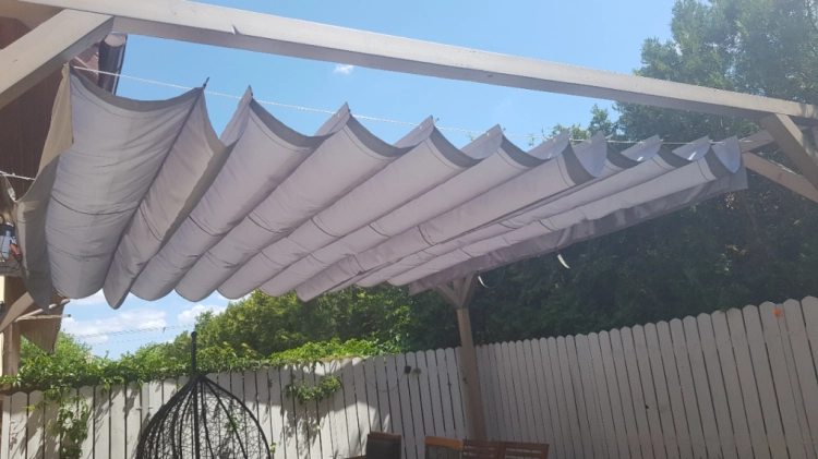 Hellgraues Premium-Raffrollo mit Sonnenschutz, montiert an einer Terrassenkonstruktion aus Holz über dem Garten