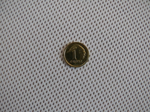 Une pièce de 1 grosz posée sur le tissu blanc d'un store romain avec une fine perforation mesh à pois