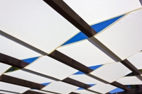 Voile d'ombrage blanche montée sur une pergola en bois sur fond de ciel