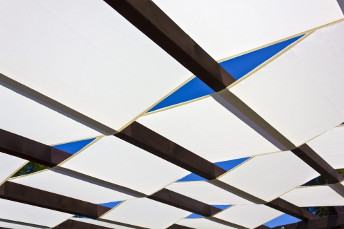 Voile d'ombrage blanche montée sur une pergola en bois sur fond de ciel