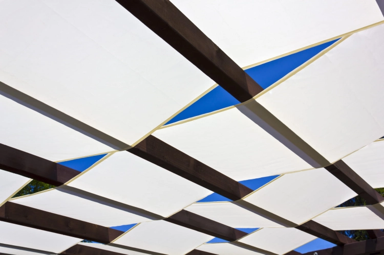 Voile d'ombrage blanche montée sur une pergola en bois sur fond de ciel