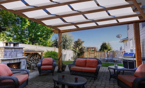 Voile d'ombrage de gazebo blanche sur une pergola en bois avec vue sur la terrasse avec meubles de jardin et cheminée
