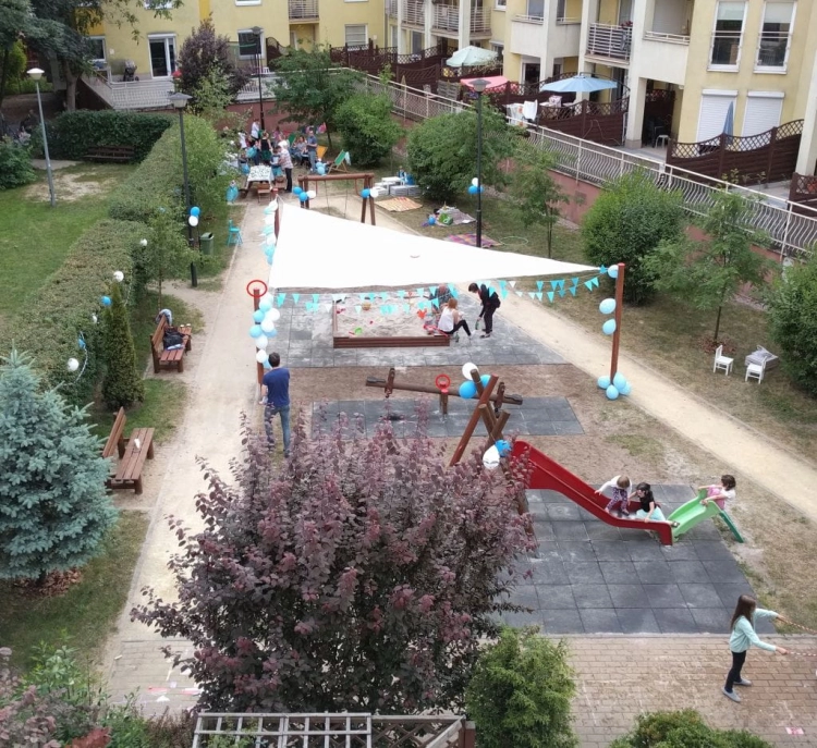 Trojúhelníková bílá stínicí plachta namontovaná nad pískovištěm na dětském hřišti u bytového domu