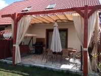 Biela záhradná clona vodotesná na mieru namontovaná v drevenej pergole na terase s relaxačným nábytkom
