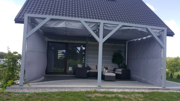 Vodotesný záhradný záves na mieru namontovaný na sivej terase so záhradným nábytkom a zastrešením