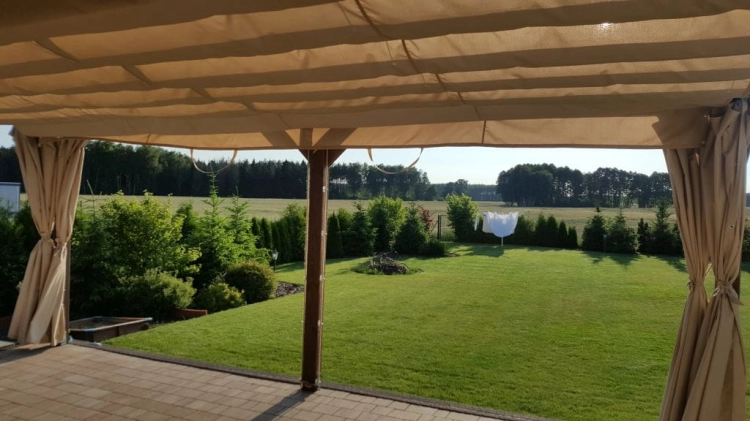 Svetlobéžové záhradné nepremokavé závesy namontované na terase s výhľadom do záhrady a na les