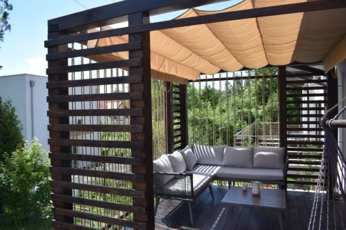 Beiges Raffrollo, sonnen- und wasserfest, nach Maß gefertigt, montiert an einer modernen Holzpergola auf der Terrasse