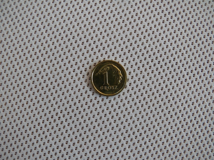Pièce de 1 grosz posée sur une bande de tonnelle blanche finement perforée
